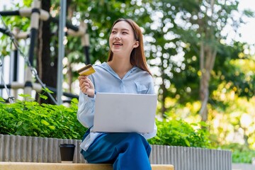 Young Asian Woman Using Laptop and Credit Card Outdoors a Modern Urban Greenery Office