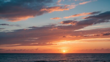 Fototapeta premium Sunset over calm ocean with colorful clouds reflecting light in a clear sky at dusk. Horizontal composition with natural scenery.