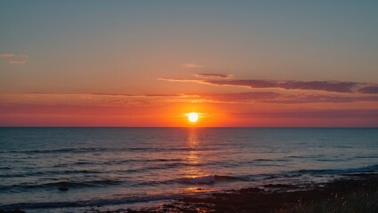 Obraz premium Sunset over calm ocean waters with vibrant colors reflecting on the surface and gentle waves lapping at the shore