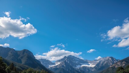 Fototapeta premium Panoramic view of snow-capped mountains under a clear blue sky with clouds and lush green forest in the foreground