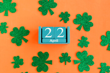 April 22. Blue cube calendar with month date and green clover leafs on bright orange background.