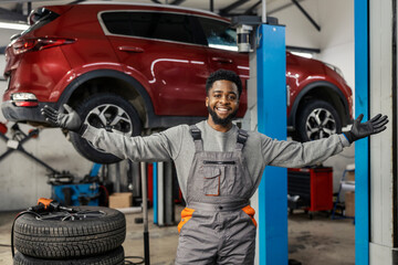 Portrait of happy multicultural car service worker smiling at camera with wide opened arms at auto...