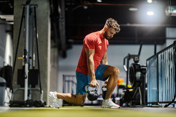 Side view of strong muscular sportsman doing lunges while carrying kettlebells at gym.