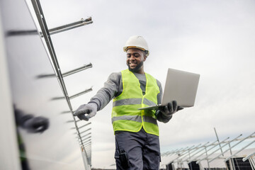 Interracial service engineer with laptop checking on solar panels at solar power plant.