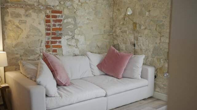 A white couch with pink pillows sits in front of a brick wall. The room has a cozy and comfortable atmosphere