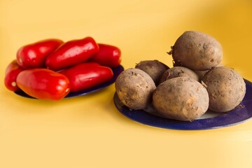 Fresh tomatoes and unpelled potatoes on the plates on yellow background.