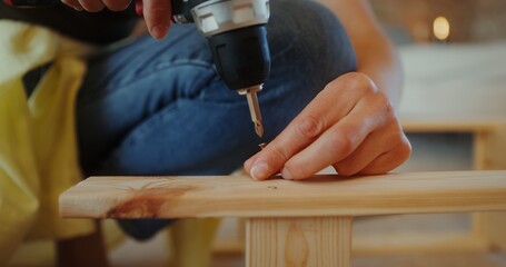 A woman assembles a wooden shelf using a screwdriver in a stylish home interior. Hands close-up, no face