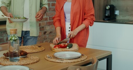 Husband and wife are getting ready for dinner. A man sets the table, a woman cuts vegetables in a stylish home kitchen