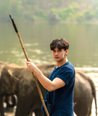 Young handsome Asian mahout holding spear weapon taking care elephant in animal conservation