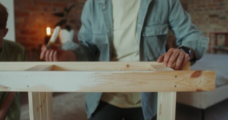 A father and son of European appearance paint a rack using brushes, sitting in a home interior,...