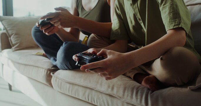 Mom and son of European appearance playing video games using joysticks sitting on the couch in a stylish home interior