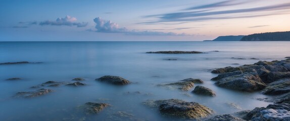 Fototapeta premium Tranquil Seascape at Dusk with Smooth Waters and Rocky Shoreline in Long Exposure Format