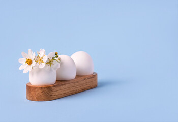 Happy Easter greeting card with place for text. Three white eggs with spring flowers of pears, strawberries and a white wreath of flowers on a blue background.