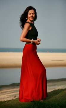 Portrait of a beautiful woman 51 years old posing in a red silk skirt and Indian earrings on the ocean shore Goa India