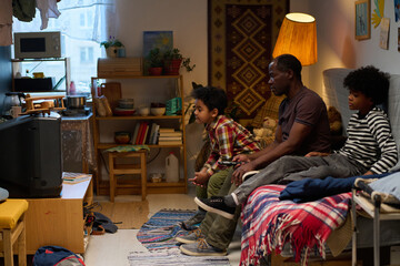 Family enjoying TV time in cozy living room with warm lighting, family members engaged in shared moment, displaying bonding in welcoming home environment