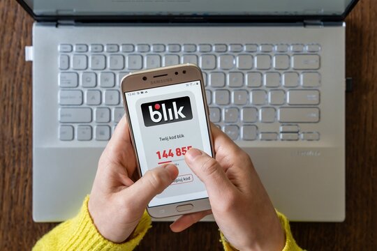 Hands holding smartphone with BLIK payment authorization code above laptop keyboard