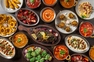 Composition from above with typical Indian dishes arranged on a dark wooden table with warm grazing light