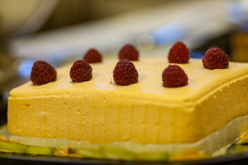 A stunning mango mousse cake beautifully garnished with plump and fresh raspberries for a delightful dessert experience
