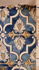 Vintage encaustic tile floor with intricate, time-worn patterns in earthy tones, featuring floral, leaf, and geometric motifs in a rustic room with high arches, lanterns, and plants.