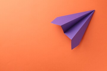 One handmade violet paper plane on orange background, top view. Space for text