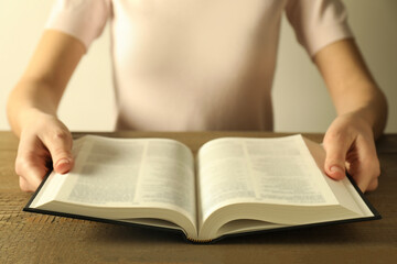 Fototapeta premium Woman reading Holy Bible in English language at wooden table, closeup