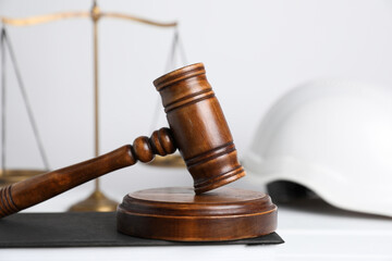 Accident at work concept. Gavel, scales and construction worker's protective gear on white wooden...
