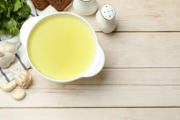 Tasty chicken bouillon in bowl with bread and ingredients on wooden table, flat lay. Space for text