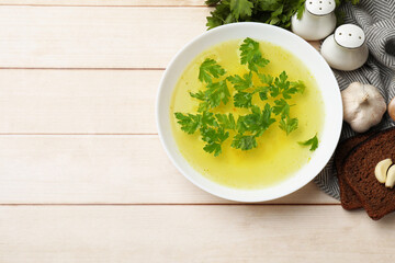 Tasty chicken bouillon in bowl with bread and ingredients on wooden table, flat lay. Space for text