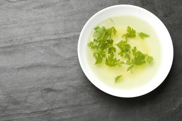 Tasty chicken bouillon with parsley in bowl on black table, top view. Space for text