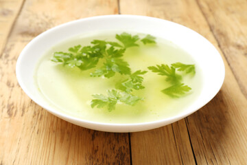 Tasty chicken bouillon with parsley in bowl on wooden table, closeup