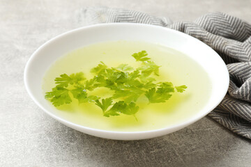 Tasty chicken bouillon with parsley in bowl on grey table, closeup