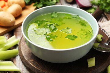 Tasty chicken bouillon in bowl and ingredients on wooden table, closeup