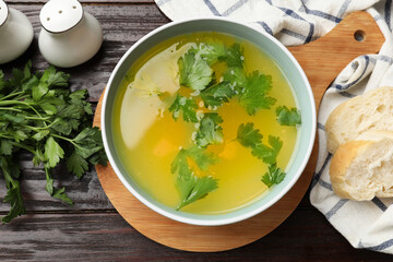 Tasty chicken bouillon in bowl, bread and ingredients on wooden table, flat lay