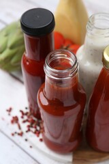 Tasty sauces in glass bottles and fresh products on white wooden table, closeup