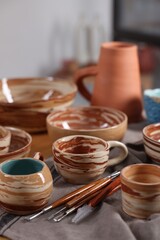 Different beautiful pottery and set of clay crafting tools on table indoors, closeup