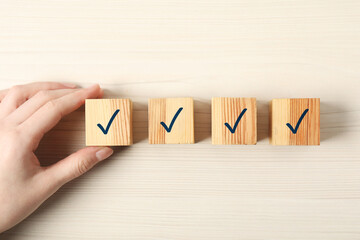 Woman taking cube with check mark at white wooden table, top view