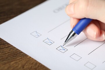 Woman checking box of paper form at wooden table, closeup