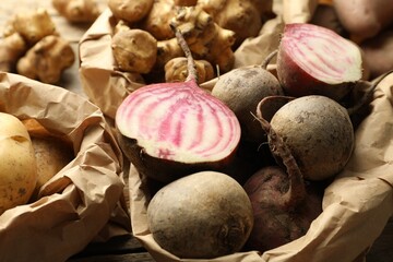 Different raw root vegetables in paper bags on table, closeup
