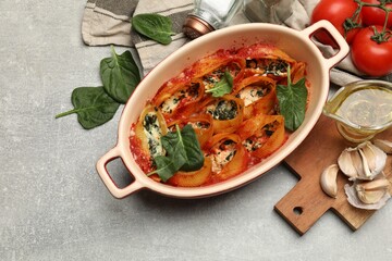 Delicious conchiglie pasta with ricotta cheese, spinach and tomato sauce in baking dish on gray textured table, flat lay