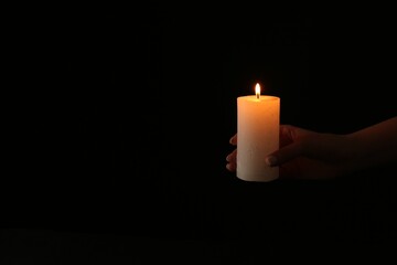 Woman with burning candle on dark background, closeup. Space for text
