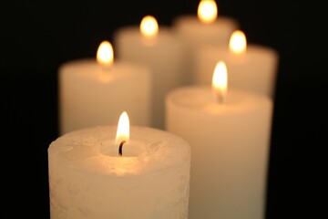 Many burning candles in darkness, closeup view