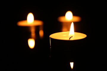 Burning candles on surface in darkness, closeup