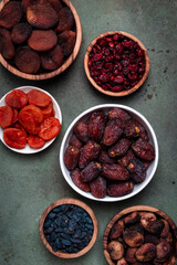 Organic sun dried fruits in bowls on green background. Healthy wholesome snacks instead of sugar and candy. Top view