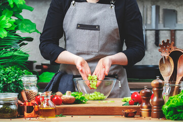 Private Chef pours chopped celery into bowl prepare Waldorf salad. Cozy kitchen with wooden table,...