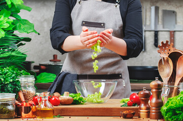 Chef pours chopped celery into bowl prepare salad. Cozy kitchen with wooden table, kitchenware,...