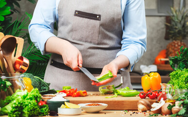 Chef cleans green paprika from seeds and membranes. Cozy kitchen with wooden table, kitchenware, vegetables, herbs and ingredients for cooking. Healthy vegan eating, culinary, recipes, food blogging