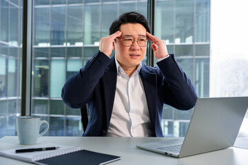 Professional businessman feeling overwhelmed while working in a modern office with glass windows, showcasing a stressful work environment and business challenges. Focused on problem-solving.