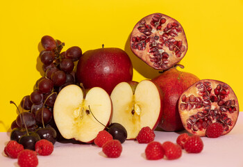 Red colored fruits. On a yellow and pink background. Monochromatic healthy food. Grapes, apples, raspberries, pomegranate