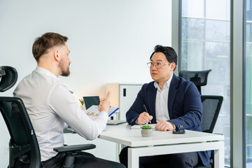 Confident businessmen engaging in a professional discussion in a contemporary office, emphasizing collaboration and strategy development. Natural lighting and business attire enhance the atmosphere.