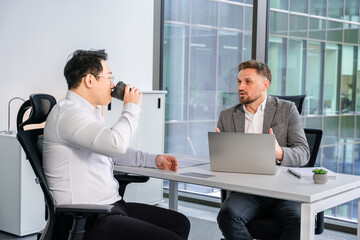 Professional businessmen conducting a formal discussion in a contemporary office setting. One is...